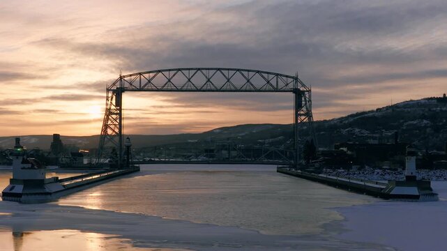 Iconic Duluth Aerial Lift Bridge centered at sunrise with winter sea smoke rising from the frozen Lake Superior ship canal in Minnesota.