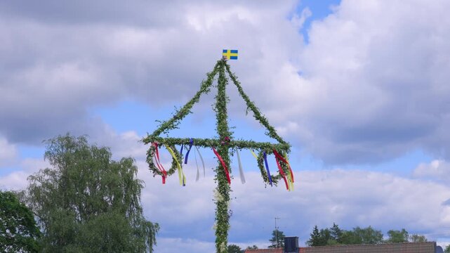 Classic Sweden Midsummer pole or maypole on sunny day in summer. Decorated with Swedish flag and greenery.. Moving slowly in light wind