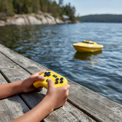Child controlling toy boat with remote at lakeside