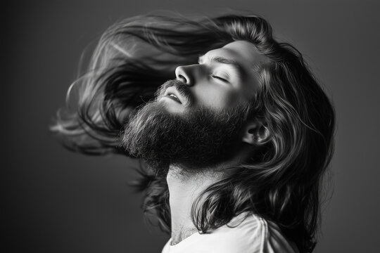 A man with long, flowing hair and a beard tilts his head back with eyes closed, capturing a moment of serenity and confidence in black and white.