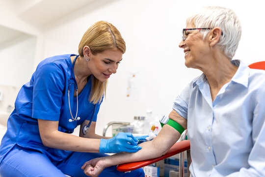 Nurse drawing blood from senior woman in clinic. Healthcare and medicine concept. Professional female phlebotomist taking blood sample from elderly patient arm for laboratory medical testing.