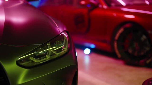 Close-up view of a modern luxury car with led headlights in an underground parking lot, showing its sleek design and vibrant, colorful lighting reflecting on its matte surface