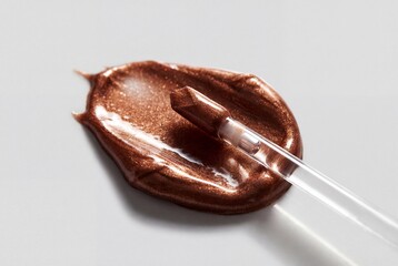 Obraz premium Metallic copper lip gloss smear with clear applicator wand on clean white background
