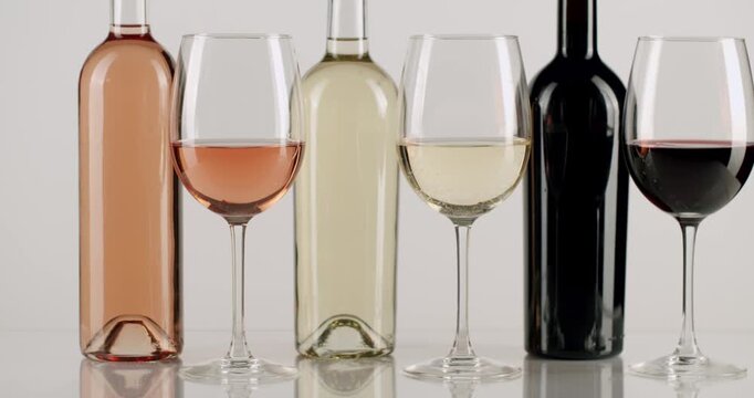 Selection of red, white, and rose wine bottles and glasses standing in a row, with the camera slowly panning from right to left, representing a wine tasting event or a cellar collection