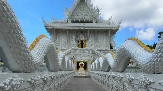 view of concrete pathway leading to white silver Buddhist temple Wat Kanan in Phuket Thailand. Sacred naga water dragons guard the road, symbol of protection, spirituality and Thai Buddhist culture