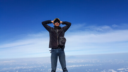 Hiker stands triumphantly above clouds under bright clear blue sky © AhmadHanif