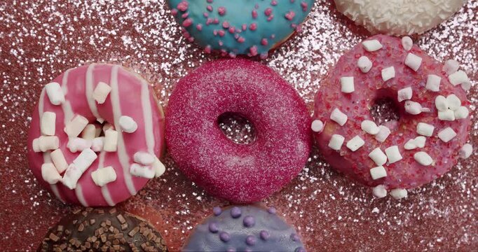 Delicious and colorful donuts with various toppings and icings on a sparkling pink background while powdered sugar gently falls, creating a sweet and festive culinary composition