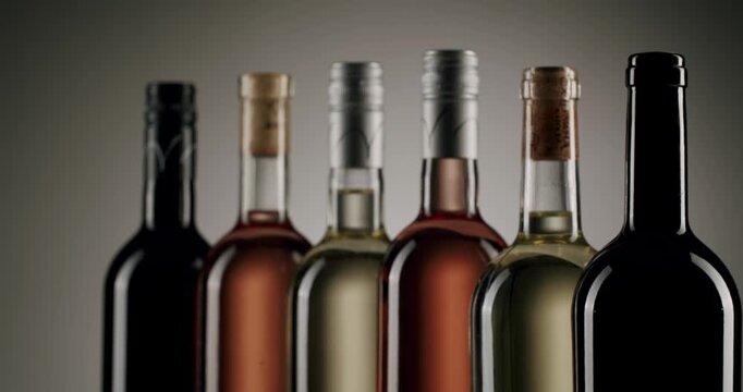 Assortment of red, rose, and white wine bottles with screw caps and cork stoppers appearing one by one in a line against a neutral background, highlighting the variety of winery production.
