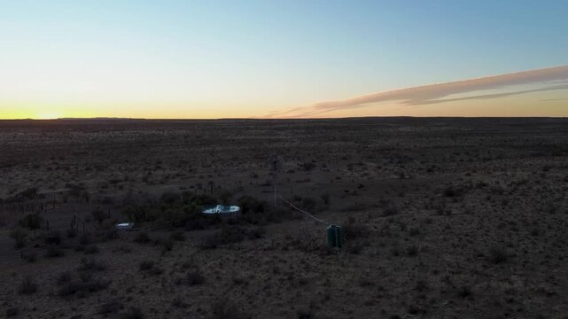 Yellow sunlight on a Wind pump and Semi-arid Karoo Landscape at sunrise, camera circling the wind pump. 4K Aerial Video.