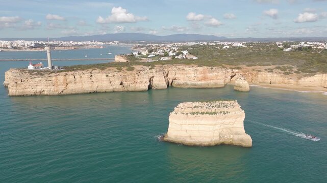 Scenic aerial shot highlighting a lighthouse perched above coastal cliffs with beaches and blue Atlantic waters below in the Algarve.