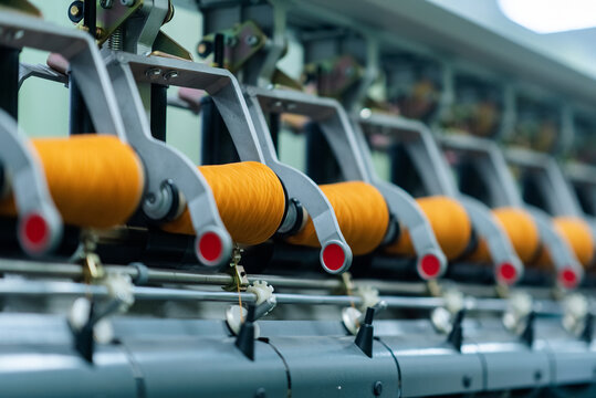 Close-up of orange yarn spools aligned on spinning machines in a textile factory