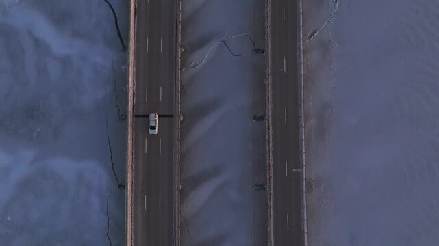 Aerial, top down view of the Robert Moses Causeway and the Great South Bay during a frozen sunset. The camera tilted down dolly in between the roads as cars drive by then tilt up to reveal the sky.