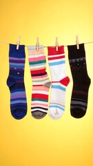 Four colorful socks hang on a clothesline with wooden pins against a bright yellow backdrop