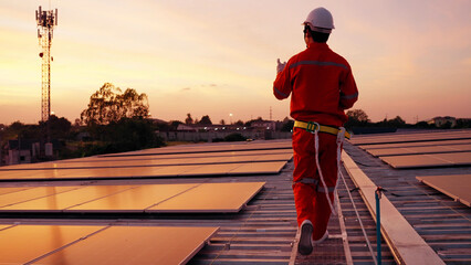 A solar technician in an orange jumpsuit walks across a rooftop solar array at sunset. Renewable energy maintenance, green infrastructure, and sustainable power solutions © comzeal