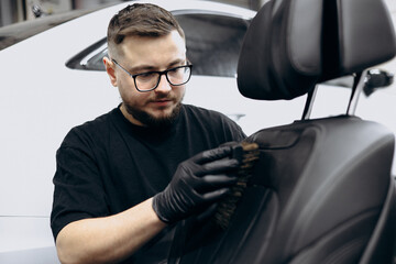Man cleaning car seat with brush and soap at car detailing service