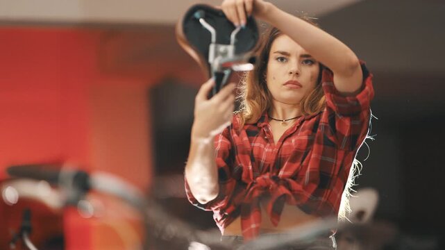 Focused woman mechanic assembling bicycle saddle in workshop