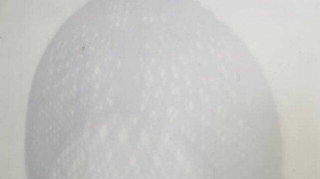 Abstract shadow of a rotating woven rattan lamp on a white wall. Minimal, organic motion background with copy space, ideal for interior design, wellness, and branding visuals.