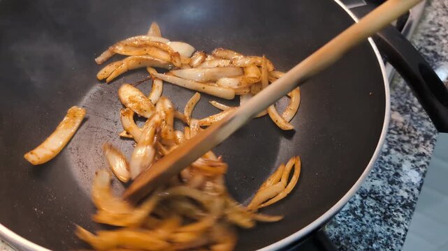 Food preparation: chopped brown onions being fried on black cast iron wok