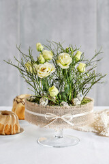 Florist at work: woman shows how to make simple Easter centerpiece with eustoma flowers, green twigs and moss in the glass stand. Step by step, tutorial.