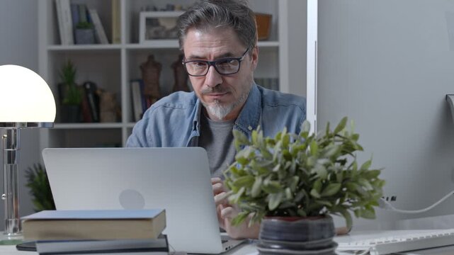 Older man working online with laptop computer at home sitting at desk. Home office, browsing internet, study room, entrepreneur.