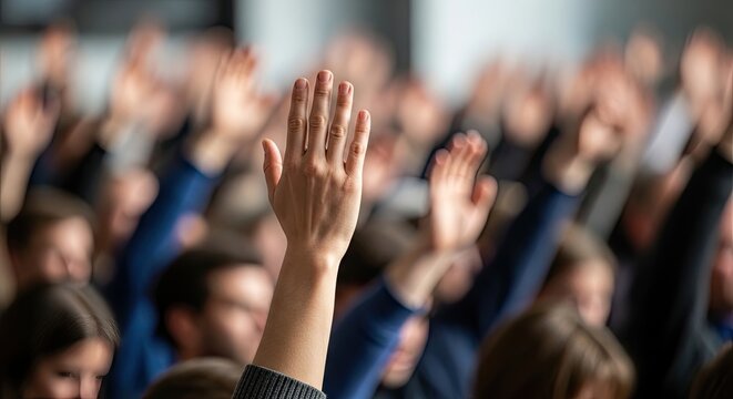 A raised hand in a crowd of people with many hands raised