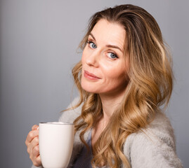 Portrait of a pretty young woman with a cup of coffee in her hands on a gray background