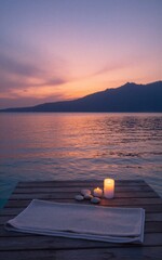 Fototapeta premium Candles, towels on wooden dock at sunset, calm lake, mountain silhouette in twilight hues.