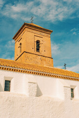 Fototapeta premium Bell tower of terracotta stones of an ancient spanish andalusian church with white stucco walls. Huebro, Almeria, Andalusia, Spain.