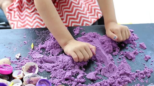 Child's hands playing with purple kinetic sand on a black table close-up