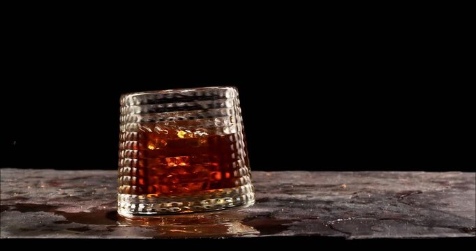 Icecube falling and splashing to glass of whiskey. Slow motion, copy space, black background. Whiskey, brandy, cognac, alcoholic drink.