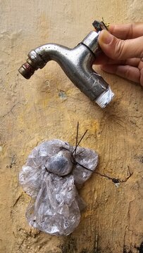 A person's hand holding a broken faucet, removed from the wall and tightly covered with plastic pipe on the wall so that water does not continue to flow from the pipe hole in the wall.