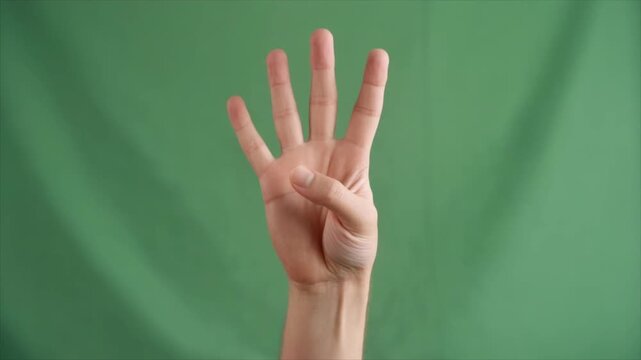 Human hand displaying the number four with four fingers up against a green backdrop, representing the concept of counting and quantity