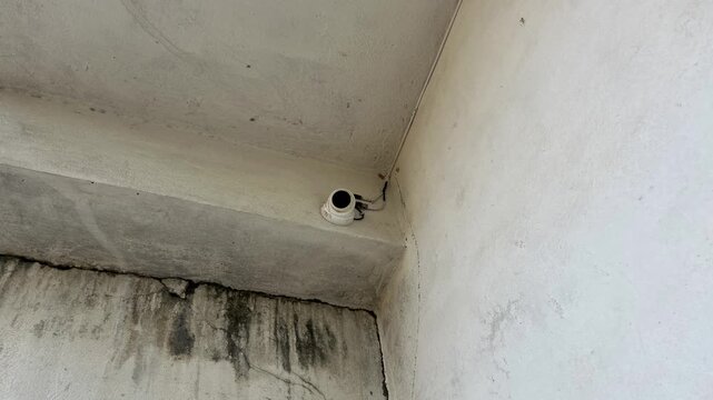 Close up of a white dome security camera installed on a concrete building wall