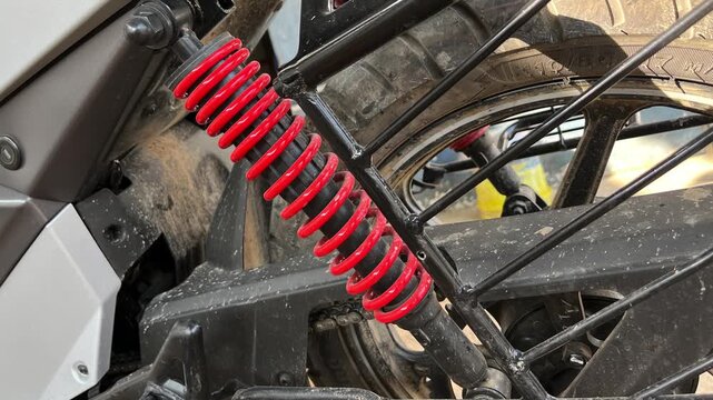Close up of a bright red coil spring rear shock absorber on a dusty modern motorcycle