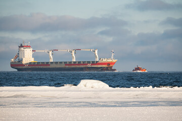 A small orange pilot boat leading a large rusty cargo ship through the blue waters of the Baltic Sea, Estonia