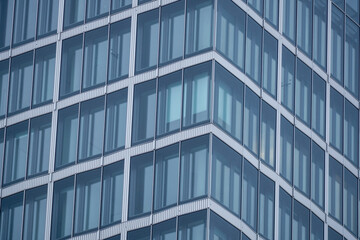 Fototapeta premium Modern glass office facade with repeating geometric window pattern, captured from below on a gray day, emphasizing lines, symmetry, and urban architecture.
