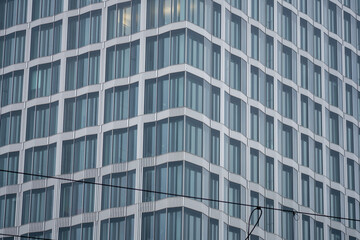 Modern glass office facade with repeating geometric window pattern, captured from below on a gray day, emphasizing lines, symmetry, and urban architecture.