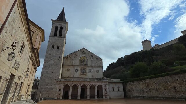 The Duomo of Spoleto features a stunning Romanesque facade, a golden mosaic, and eight rose windows. The portico and bell tower create a majestic silhouette against the Umbrian sky