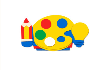 Colorful art supplies arranged in a creative layout showing a paint palette, pencils, and a light bulb on a white background in a studio setting