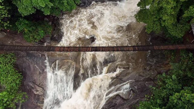 The image showcases Bambarakiri Ella Falls, a picturesque 3-meter waterfall near Rattota in Matale, Sri Lanka, surrounded by lush evergreen forest and featuring a charming suspension bridge