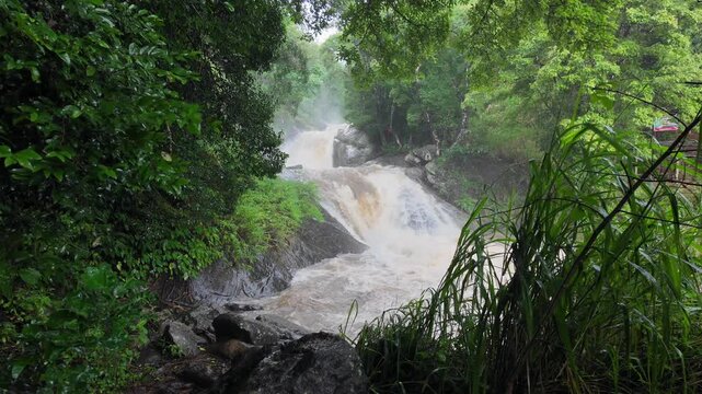 The image showcases Bambarakiri Ella Falls, a picturesque 3-meter waterfall near Rattota in Matale, Sri Lanka, surrounded by lush evergreen forest and featuring a charming suspension bridge