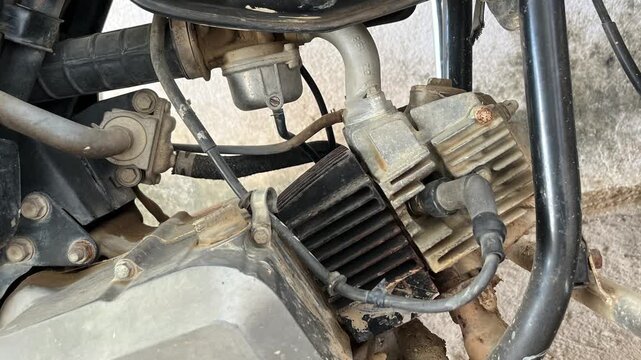 Close up of a dusty single-cylinder motorcycle engine showing cooling fins, spark plug cable, and carburetor