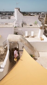 Static video of a woman stepping onto her terrace with a basket of freshly picked lemons and lying down on a sun lounger. Mediterranean everyday life, warm light, calm routine and peaceful slow living