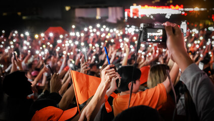 Fototapeta premium Close up of a hand holding a pen ready for voting at a People's Party rally in Thailand. Supporters with orange flags and phone lights in background for February 8, 2026 election.