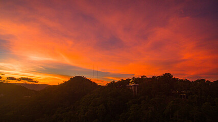 Fototapeta premium Aerial view of scenery Khao Rang viewpoint at twilight. view of a town nestled among lush green mountains at sunset, with a Pavilion structure perched on the hillside at Phuket town at Dusk