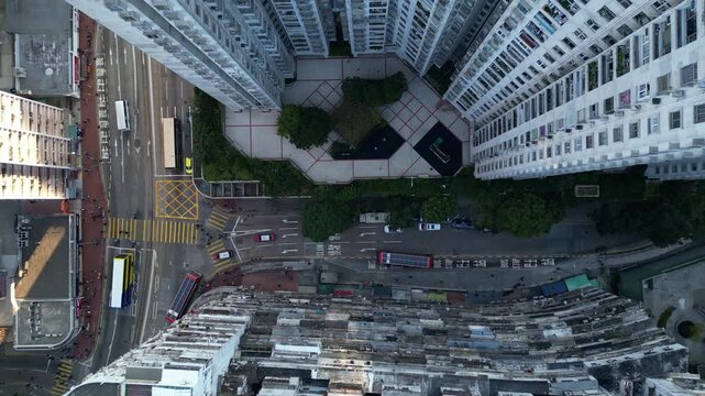 Top down view of stacked facades around deep courtyard with buses and trams moving along junction below. Rooftops show tanks pipes vents and weathered texture of old Hong Kong