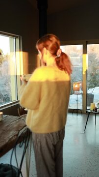 Calm lifestyle video of a woman entering the frame and drinking coffee inside a modern mountain house. Warm natural light, peaceful atmosphere, slow living concept, cozy interior and quiet moment of
