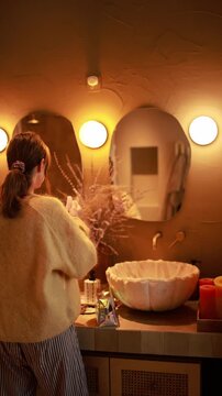 Slow living video of a woman applying skincare during a calm morning routine in a luxury bathroom. Warm ambient lighting, organic textures, minimalist interior and relaxing self care atmosphere