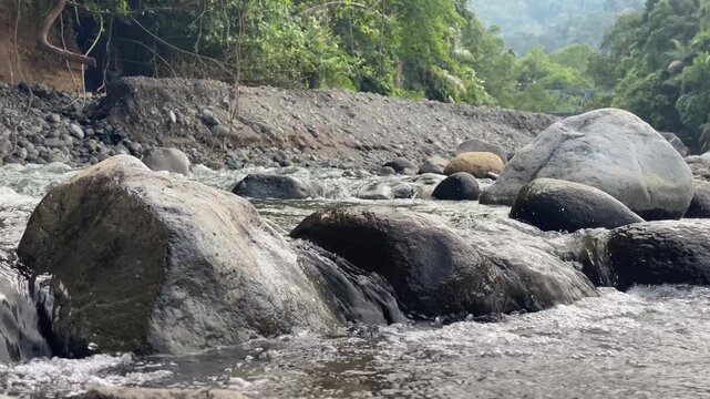 river in the forest , Tropical River Flowing Over Large Rocks in Lush Green Forest , A serene landscape featuring a clear mountain river cascading over smooth large boulders. The background shows a lu