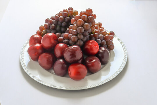 Cachos de uvas roxas e figos frescos sob um prato, isolados em um fundo branco.